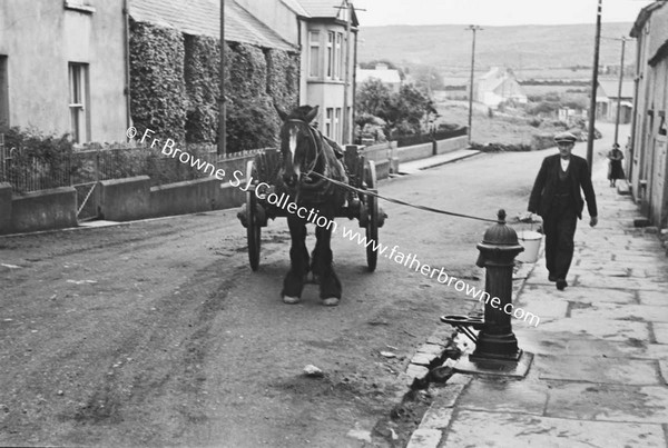 MAN LEADING HORSE AND CART UP STREET